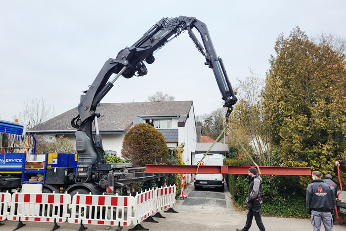 Eine große Baumaschine auf einer Straße, die einen roten Stahlträger transportiert.